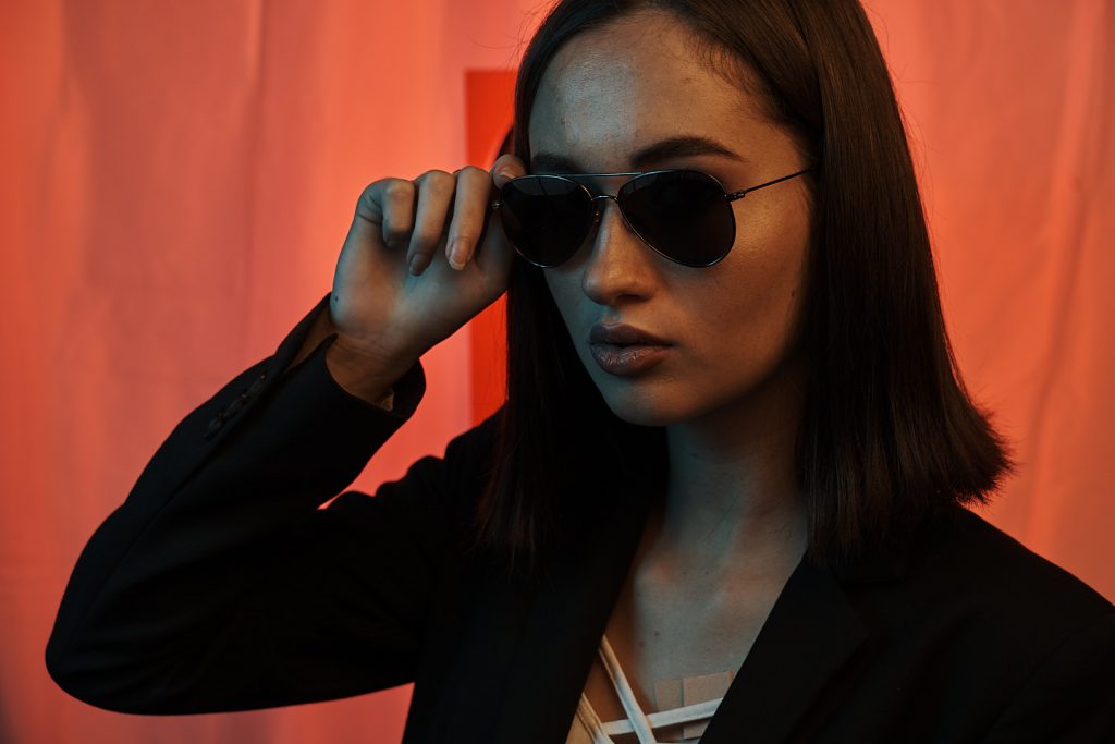 Portrait fashion d'un model avec lunette sur un fond sombre et coloré photo brute