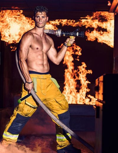 Photos pompier artistique tenant une lance eau avec le feu en arrière plan