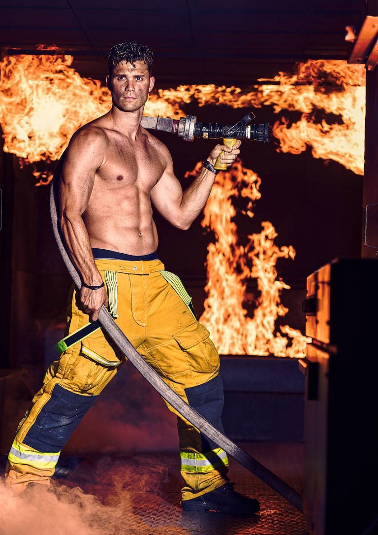 Photos pompier artistique tenant une lance eau avec le feu en arrière plan